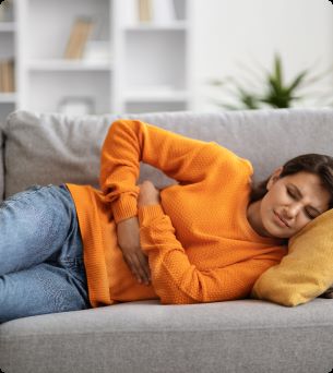 Vrouw in oranje trui met buikpijn op de bank